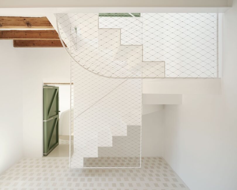 Una escalera blanca con líneas geométricas, barreras de malla de seguridad, puertas verdes, vigas de madera en el techo y baldosas claras estampadas evocan un diseño interior minimalista que recuerda a la leche desnatada.