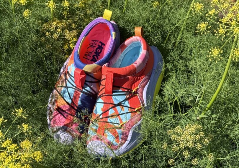 Un par de coloridas zapatillas para correr Hoka Propar que aparecen entre los diez mejores estilos de 2025, frente a hojas verdes y flores amarillas bajo la luz del sol.