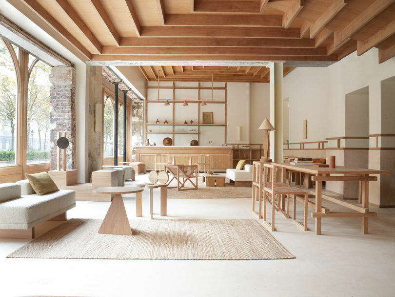 El amplio y moderno salón cuenta con techos con vigas de madera, muebles sencillos de madera clara, grandes ventanales y una decoración en tonos neutros.