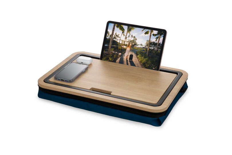 Una tableta que muestra una escena tropical y un teléfono inteligente con auriculares descansan sobre un escritorio de madera con una base de cojín azul.