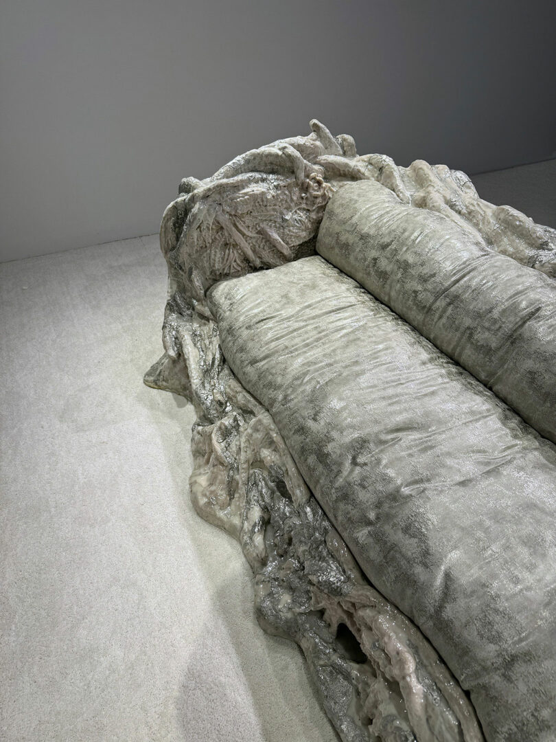 Un escultural sofá metálico con una base orgánica similar a una roca descansa sobre una alfombra clara y se apoya contra una pared lisa.