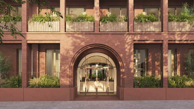 Esta imagen muestra el exterior de ladrillo del edificio Brent Barker, con una gran entrada arqueada, un balcón y vegetación en las ventanas y la entrada.