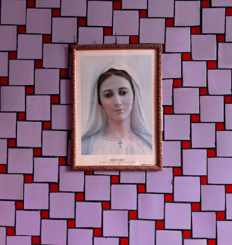 Un retrato enmarcado de la Virgen María de Maye Ruiz cuelga de una pared geométrica de color púrpura y rojo.