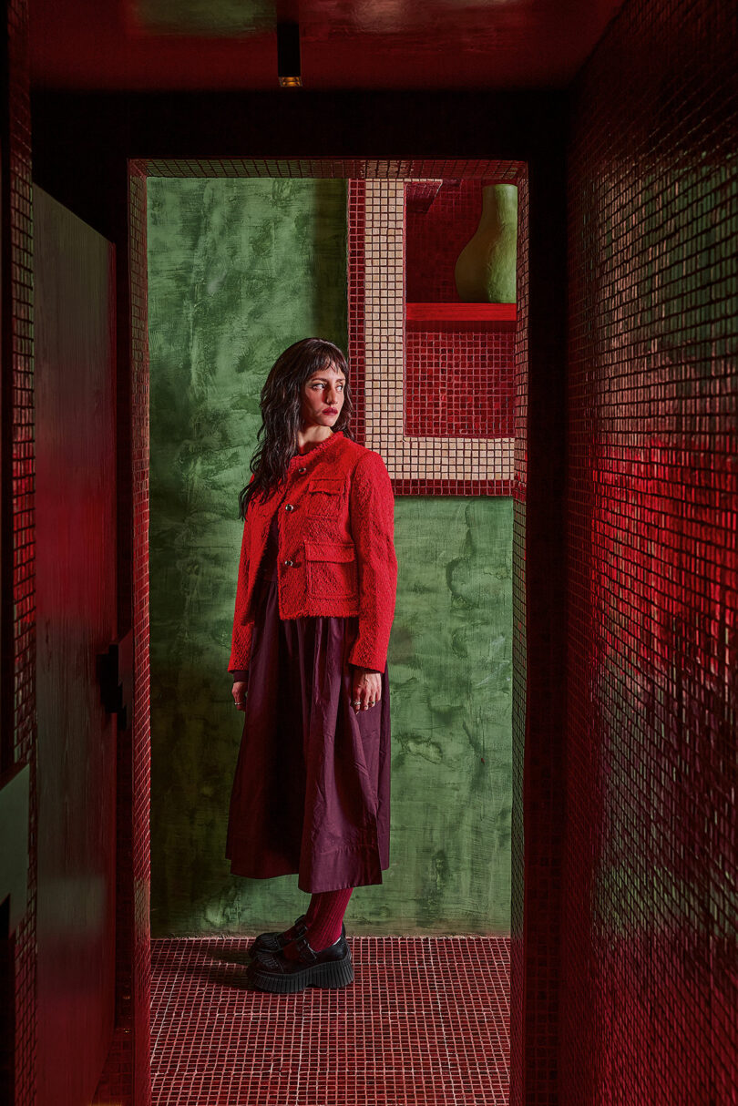 Maye Ruiz, vestida con una chaqueta roja y una falda larga, estaba parada en un pasillo estrecho, de azulejos rojos y paredes verdes, y miró a su izquierda.