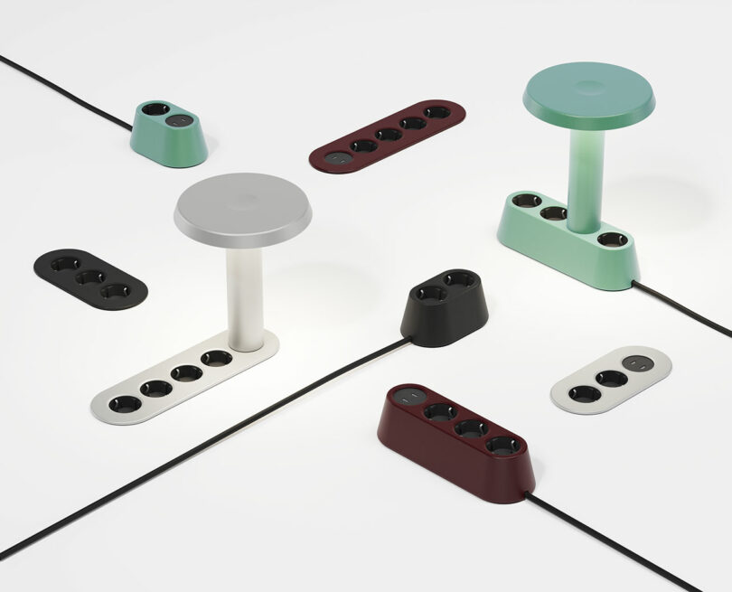 Sobre la superficie blanca se encuentran varias regletas de estilo moderno y pequeñas lámparas de mesa de diferentes colores, con cables que se extienden hacia afuera.