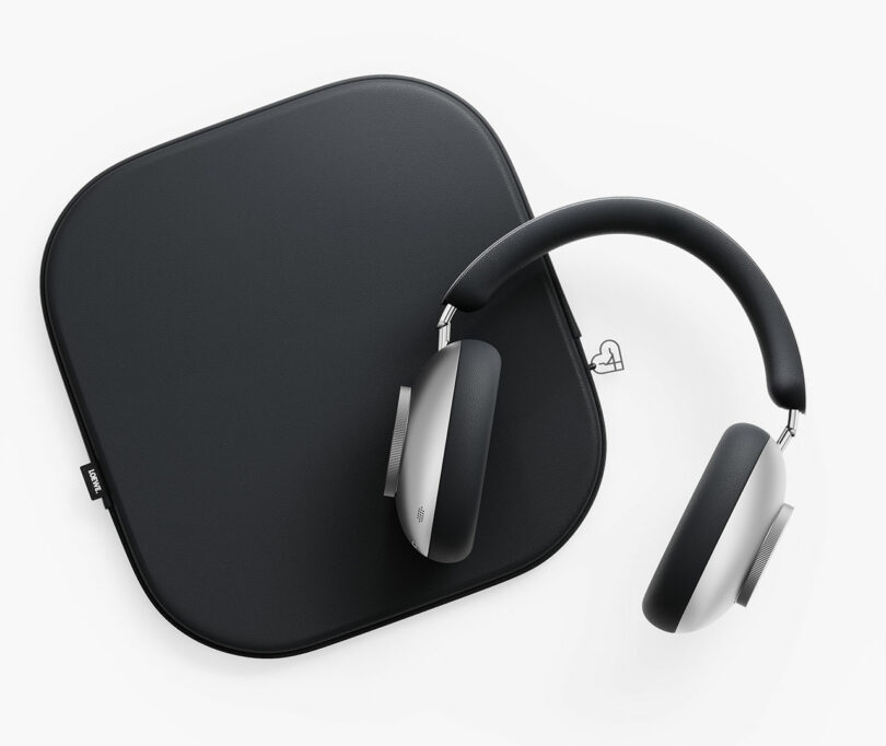 Un par de auriculares supraaurales con un diseño elegante y moderno que descansan parcialmente sobre un estuche cuadrado negro sobre un fondo blanco.