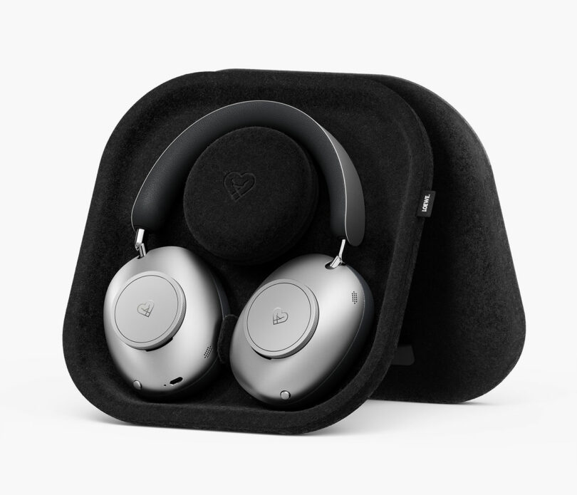 Los auriculares inalámbricos supraaurales plateados se muestran en un soporte contorneado negro con un logotipo de corazón tanto en los auriculares como en el soporte.