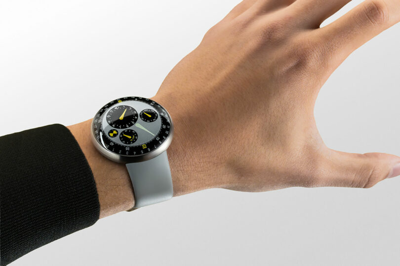 A person wearing a TYPE 3 silver round-faced wristwatch with a gray band and multiple small dials on the watch face.