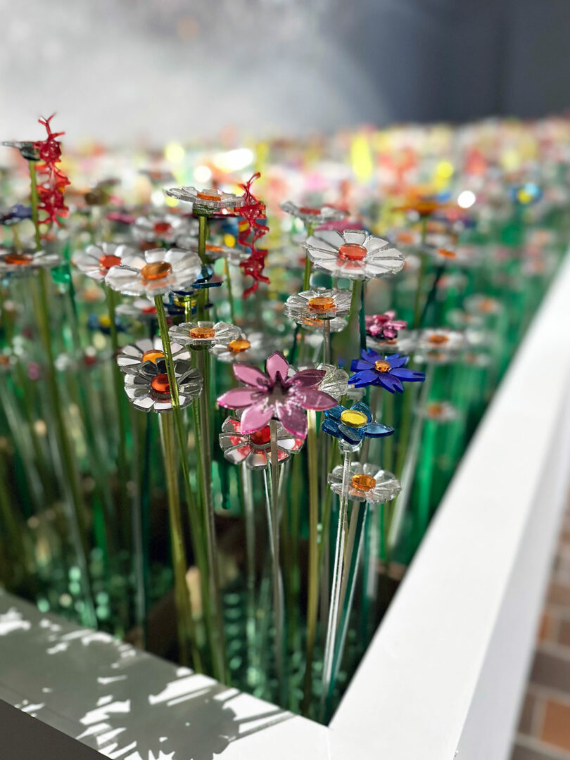 A display of colorful artificial flowers made from plastic and metal, arranged upright in a rectangular planter, beautifully reflecting diversiveness mo man tai.