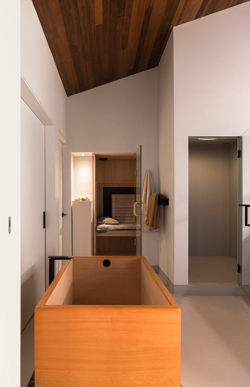 La moderna sala de spa cuenta con una bañera de madera, una sauna al aire libre forrada con toallas y una decoración minimalista con acabados en madera y blanco.