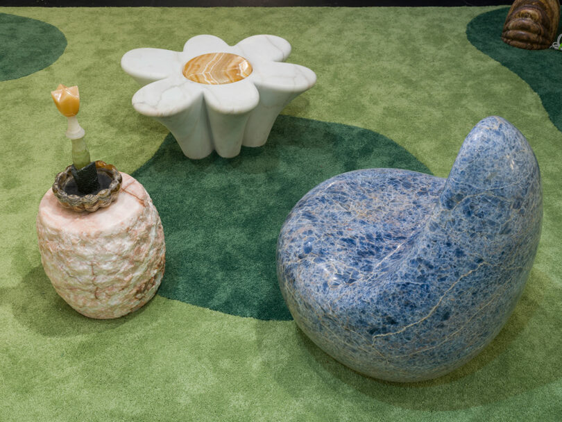 Sillas redondas de piedra azul, una mesa auxiliar de piedra rosa adornada y una mesa de centro blanca con forma de flor de Sten Studio se sientan elegantemente sobre una alfombra estampada verde.