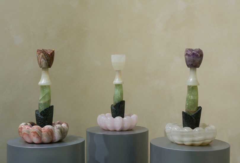 Tres piezas escultóricas de Sten Studio presentan piedras de colores apiladas sobre pedestales circulares contra paredes de color beige claro. Cada escultura tiene una base en forma de flor y una parte superior en forma de tulipán.