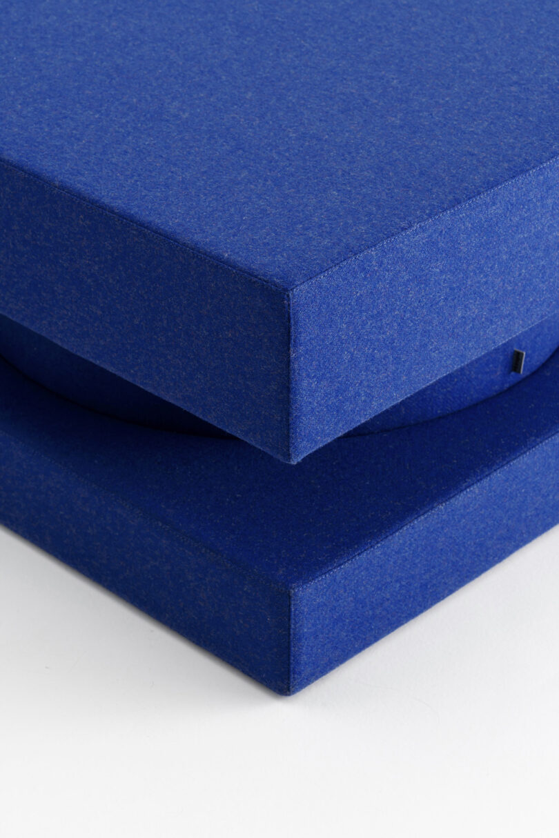 A close-up of a blue hardcover book stacked on top of another blue book, both lying on a white surface.