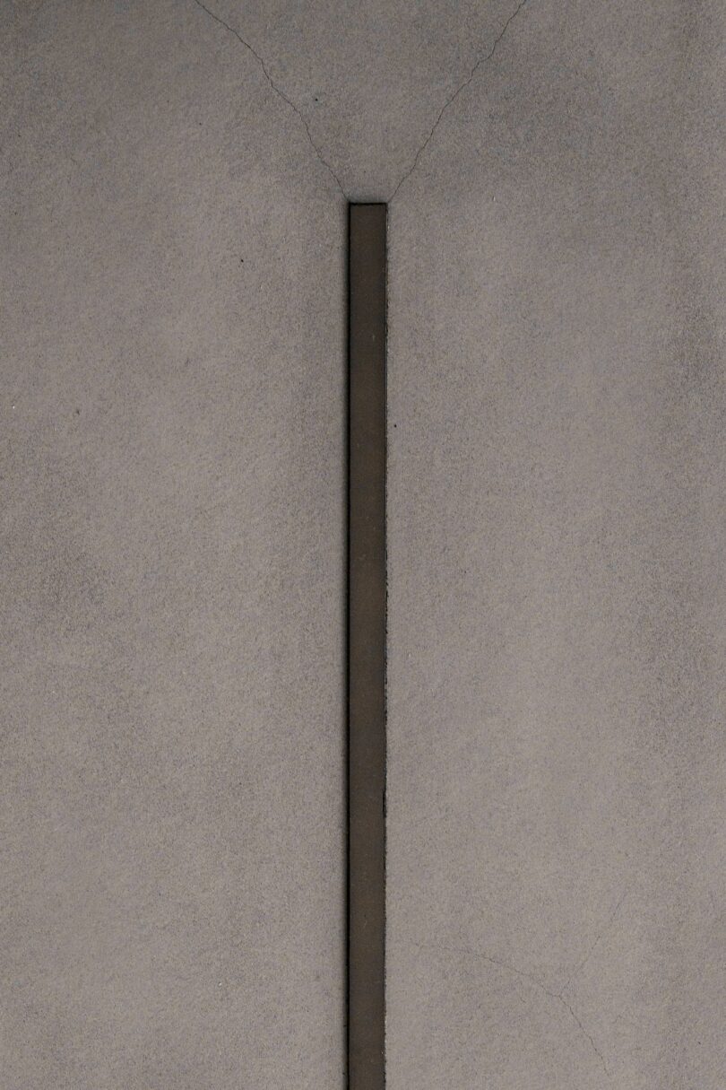 En el centro de la superficie de hormigón gris se encuentra una franja vertical y estrecha de color oscuro, con sutiles grietas que irradian hacia afuera.