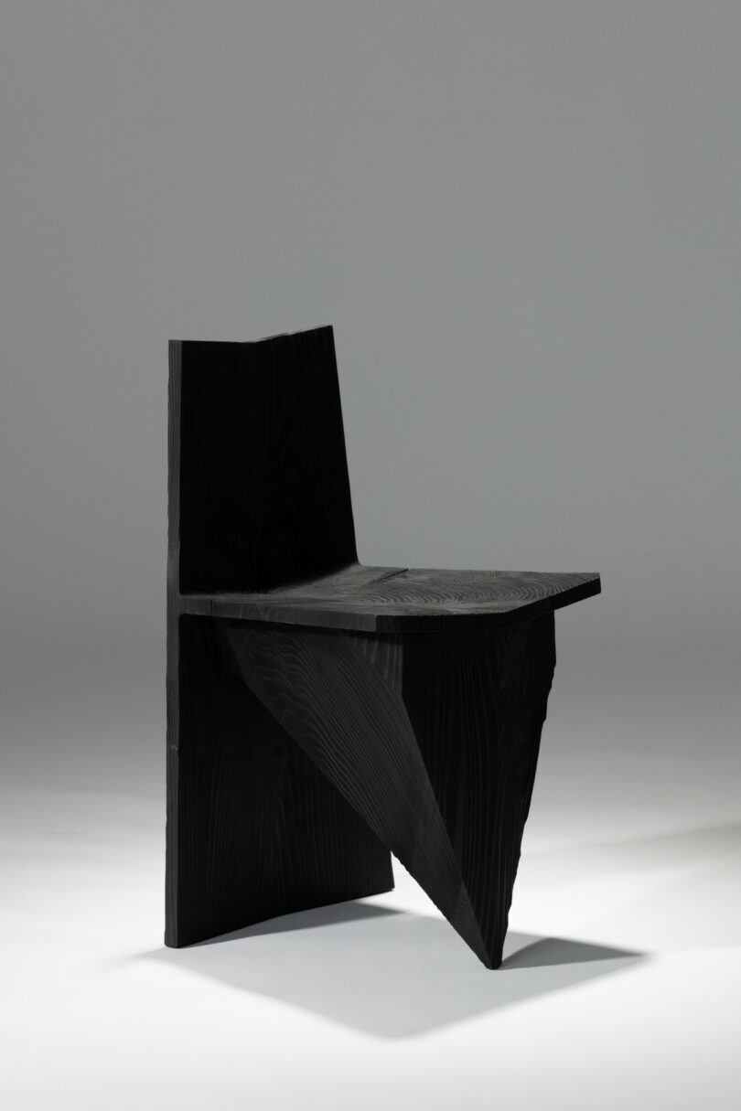 Una silla negra y angular con formas geométricas y bordes afilados, fotografiada sobre un sencillo fondo gris claro.