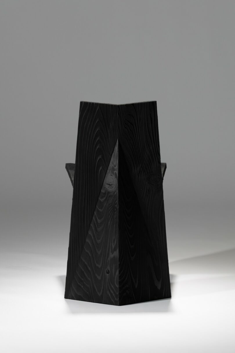 Una silla negra y angular con formas geométricas y bordes afilados, fotografiada sobre un sencillo fondo gris claro.