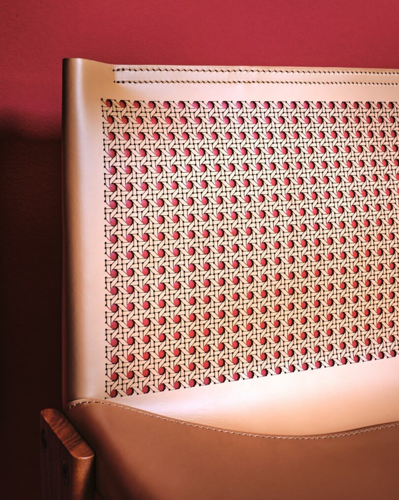 Primer plano del respaldo de una silla con bordes de cuero color canela y un intrincado patrón de ratán tejido contra una pared rojiza