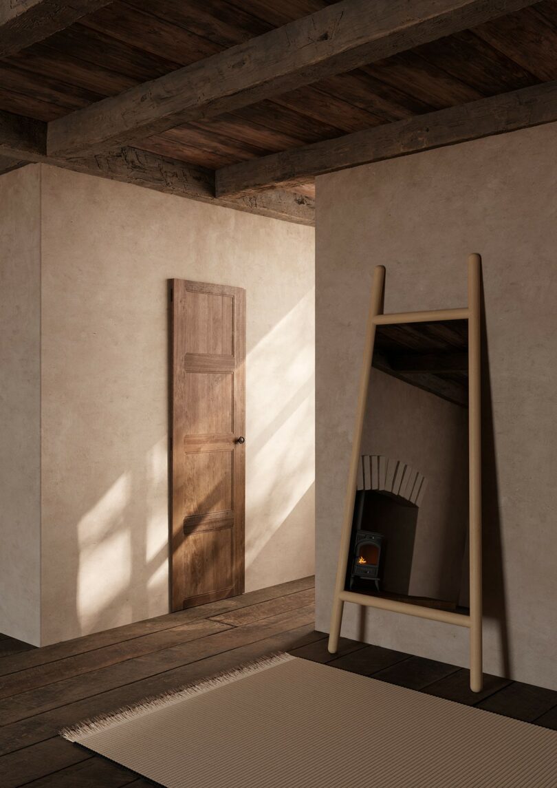Una habitación rústica con pisos y vigas de madera en el techo, una puerta de madera cerrada, un espejo en el piso inclinado y una pequeña chimenea vista en el reflejo