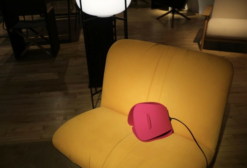 Una silla de color amarillo brillante con una bolsa rosa en el asiento se coloca en una habitación con pisos de madera e iluminación tenue.
