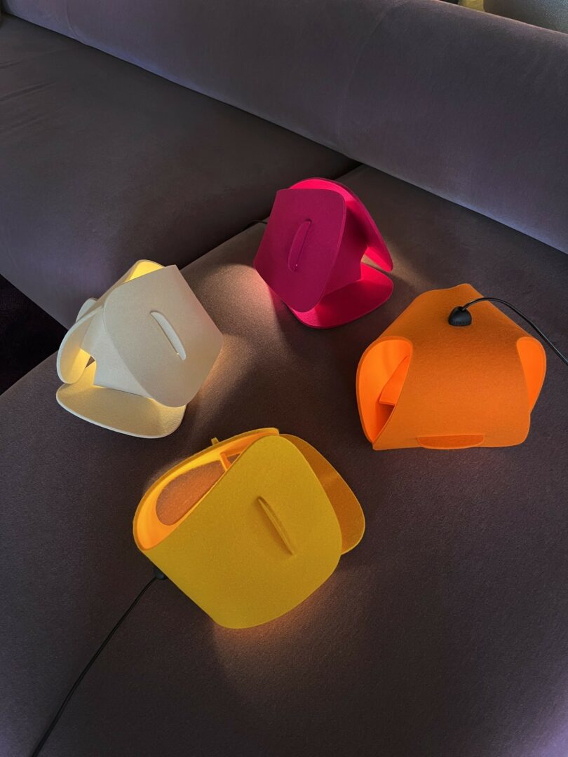 Cuatro coloridos bolsos geométricos hechos de tela se colocan sobre un sofá marrón. Los colores de la bolsa incluyen amarillo, crema, rosa brillante y naranja.