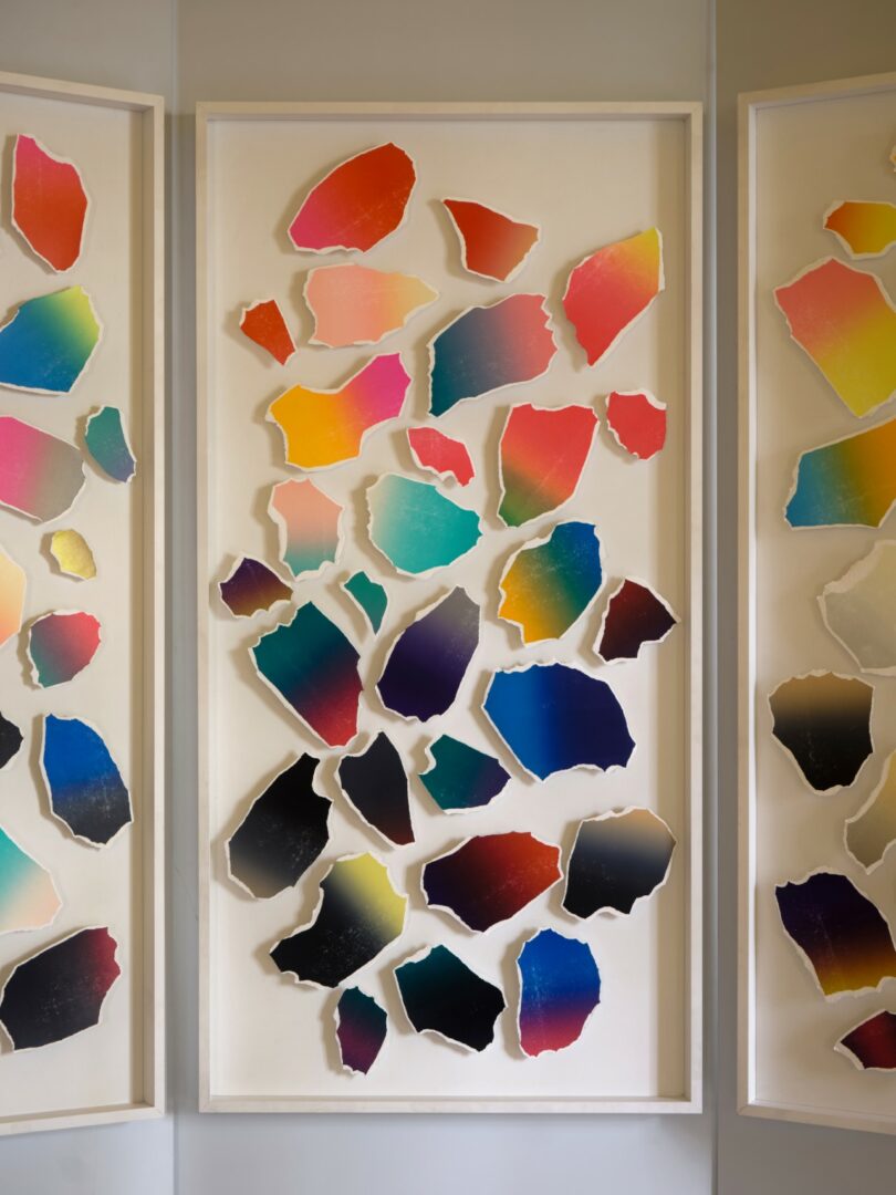 Interior luminoso con arte mural clásico y suelo de mármol, tres paneles blancos plegados que muestran coloridas formas abstractas