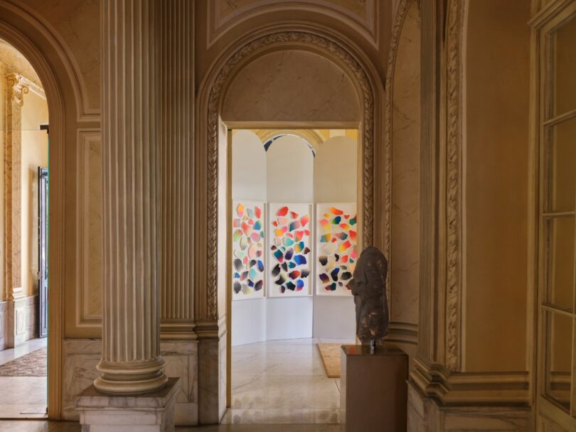 La vista a través de la entrada arqueada es de una habitación luminosa con arte abstracto colorido en las paredes y un busto de piedra sobre un pedestal en primer plano.