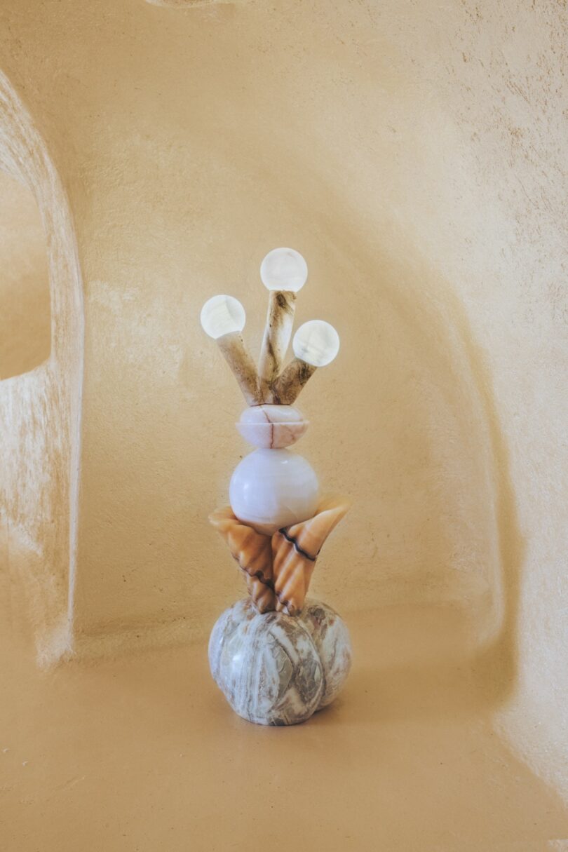 Disposición escultórica de conchas, piedras y objetos con forma de cuerno apilados verticalmente sobre fondo beige texturizado