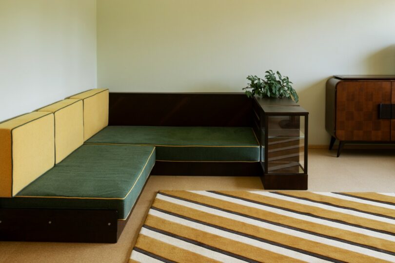 Salón moderno de mediados de siglo con sofá seccional verde y amarillo, mesa auxiliar con plantas, armarios de madera y alfombra a rayas beige y marrón