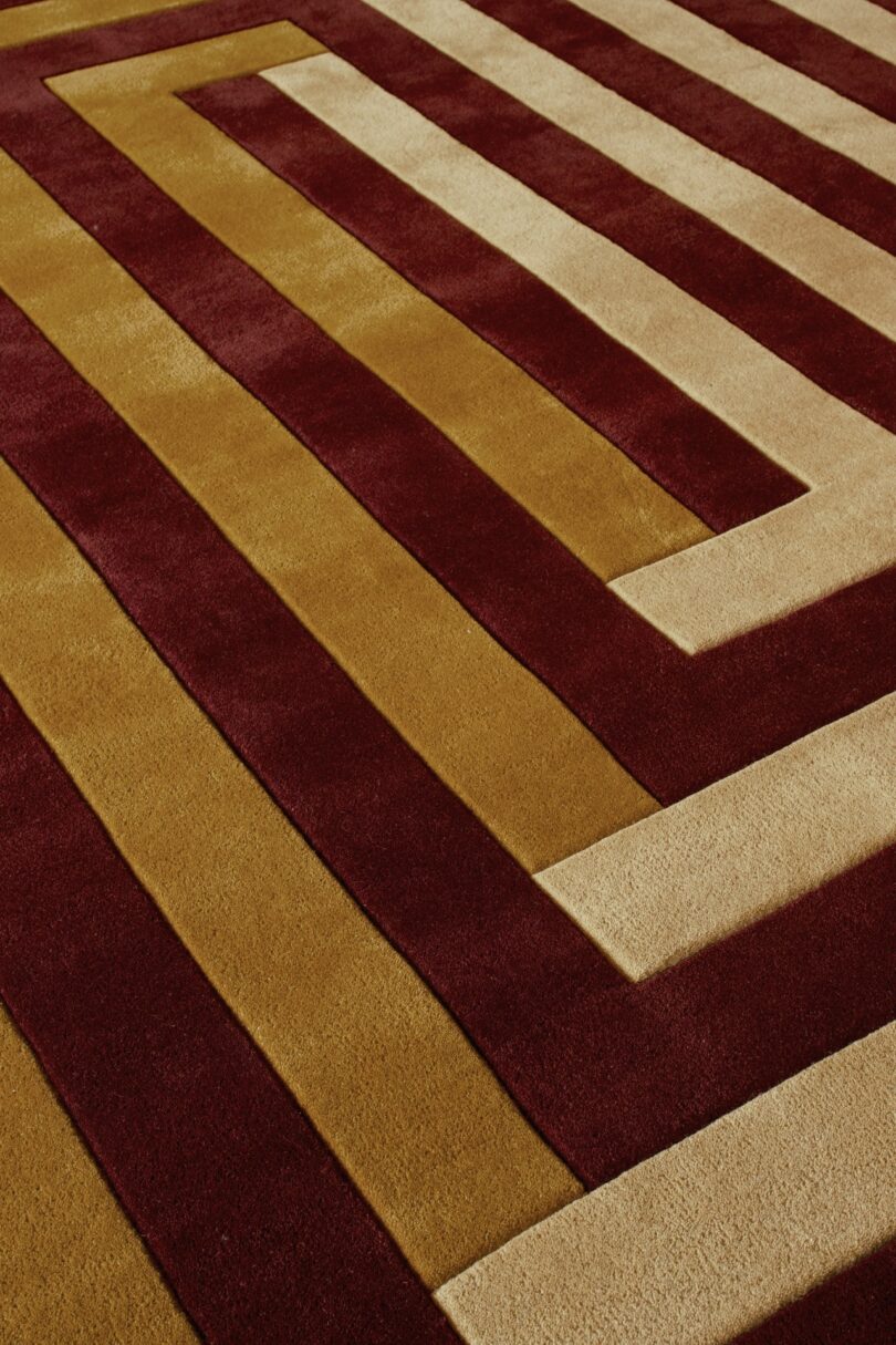Alfombra con motivos geométricos con bandas rectangulares alternas de color granate, dorado y beige formando un diseño en zigzag