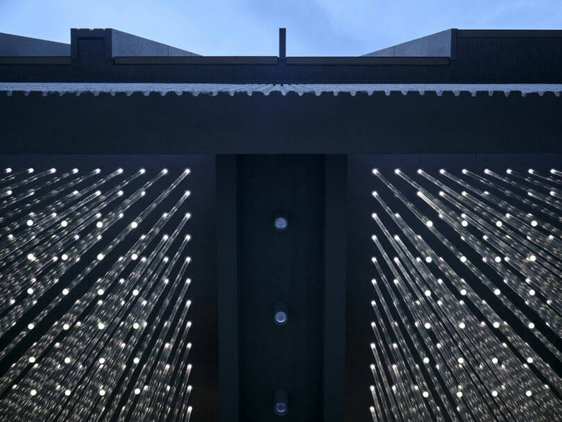 La vista simétrica mira hacia el techo, donde filas de barras de luz brillantes espaciadas uniformemente se extienden hacia abajo, contra la estructura oscura del edificio y el cielo azul.