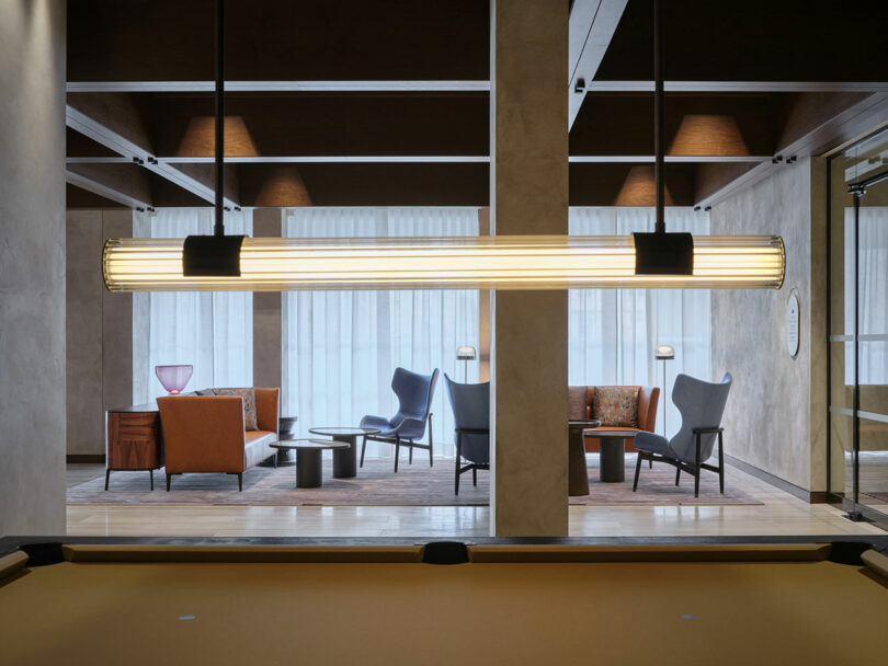 La moderna sala de estar está amueblada con sillones, sofás, mesas y lámparas de pie, que son visibles a través de las mamparas y las lámparas lineales colgantes detrás de la mesa de billar.