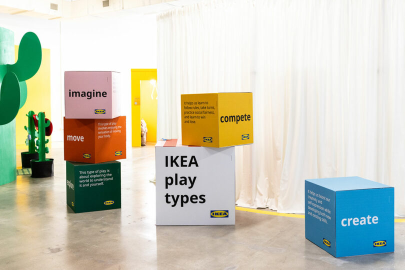 Big colored cubes with motivational words like "imagine," "move," "compete," and "create" displayed in a modern, minimal interior with a white curtain and colorful decoration.
