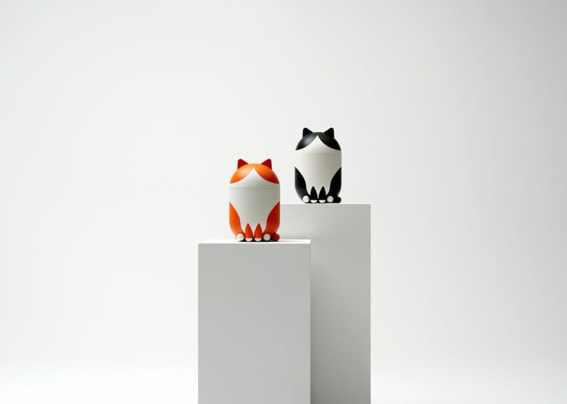Two geometric fox-shaped figures—one orange and one black—appear on separate white pedestals against a plain white background.