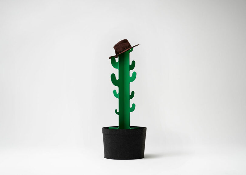 A green, stylized cactus in a black pot with a brown hat placed on top, on a plain white background.