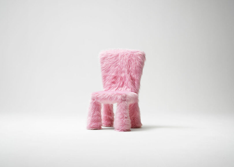 A chair covered in fluffy pink faux fur stands against a white, minimalist backdrop.