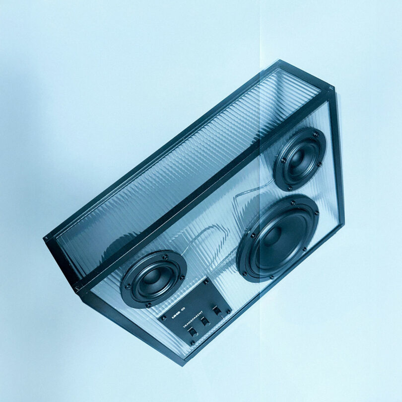 Altavoz transparente con componentes internos visibles, incluidos dos controladores de medios, un woofer y un panel de control, con fondo azul claro.