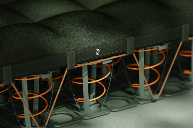 Vista cercana de una sección transversal de un colchón, que muestra material de amortiguación verde, resortes helicoidales de color naranja y soportes estructurales debajo.