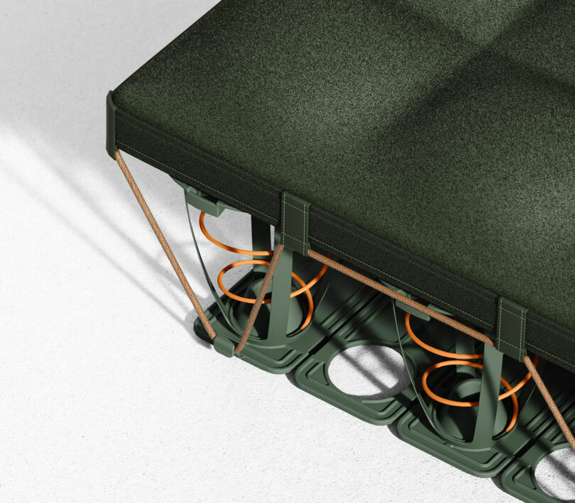 Primer plano de las esquinas de un colchón verde que muestra los resortes internos de color naranja y la estructura de soporte sobre una superficie blanca.