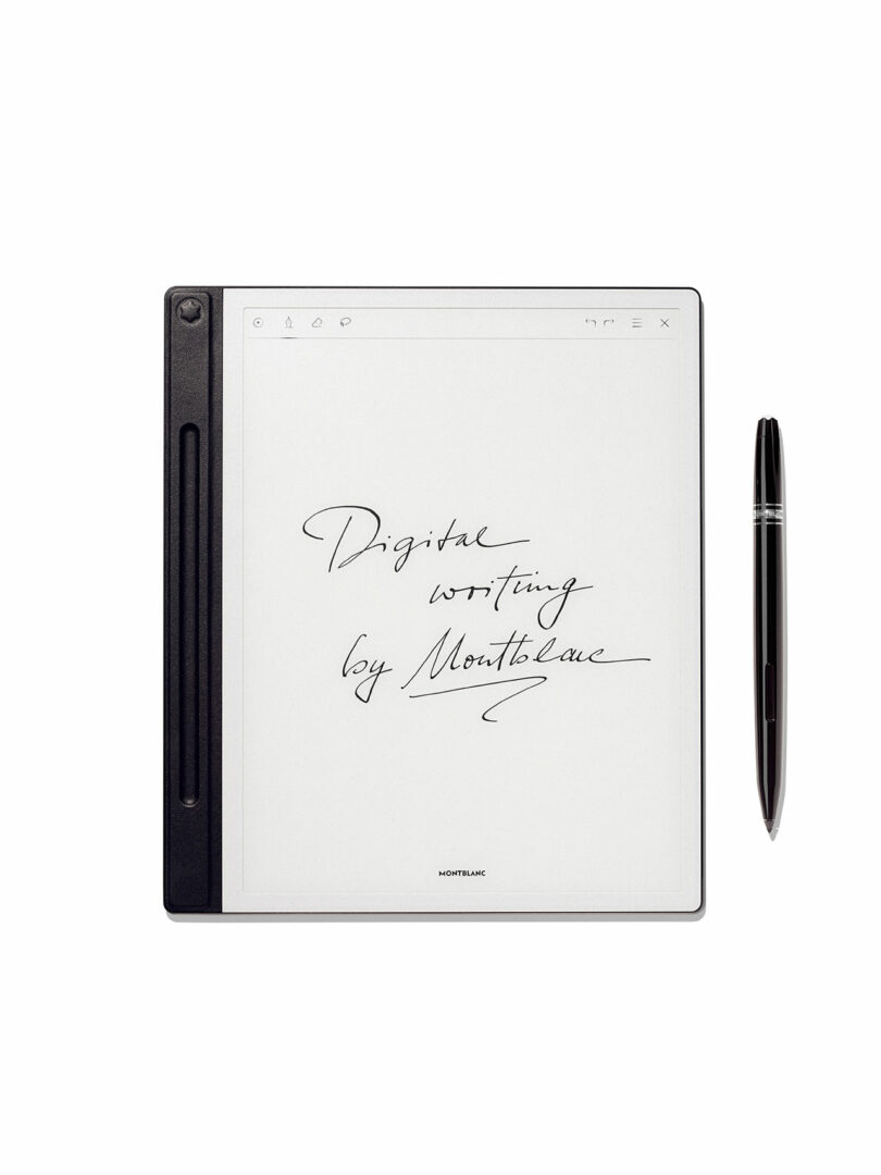 A digital notepad with handwritten text "Digital writing by Montblanc" on the screen, designed in collaboration with Fuseproject, alongside a black stylus pen placed to the right.