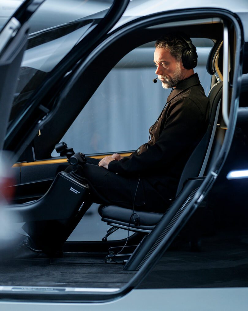 Un hombre con auriculares se sienta en la cabina de un avión o simulador moderno y mira desde un lado a través de la puerta abierta.