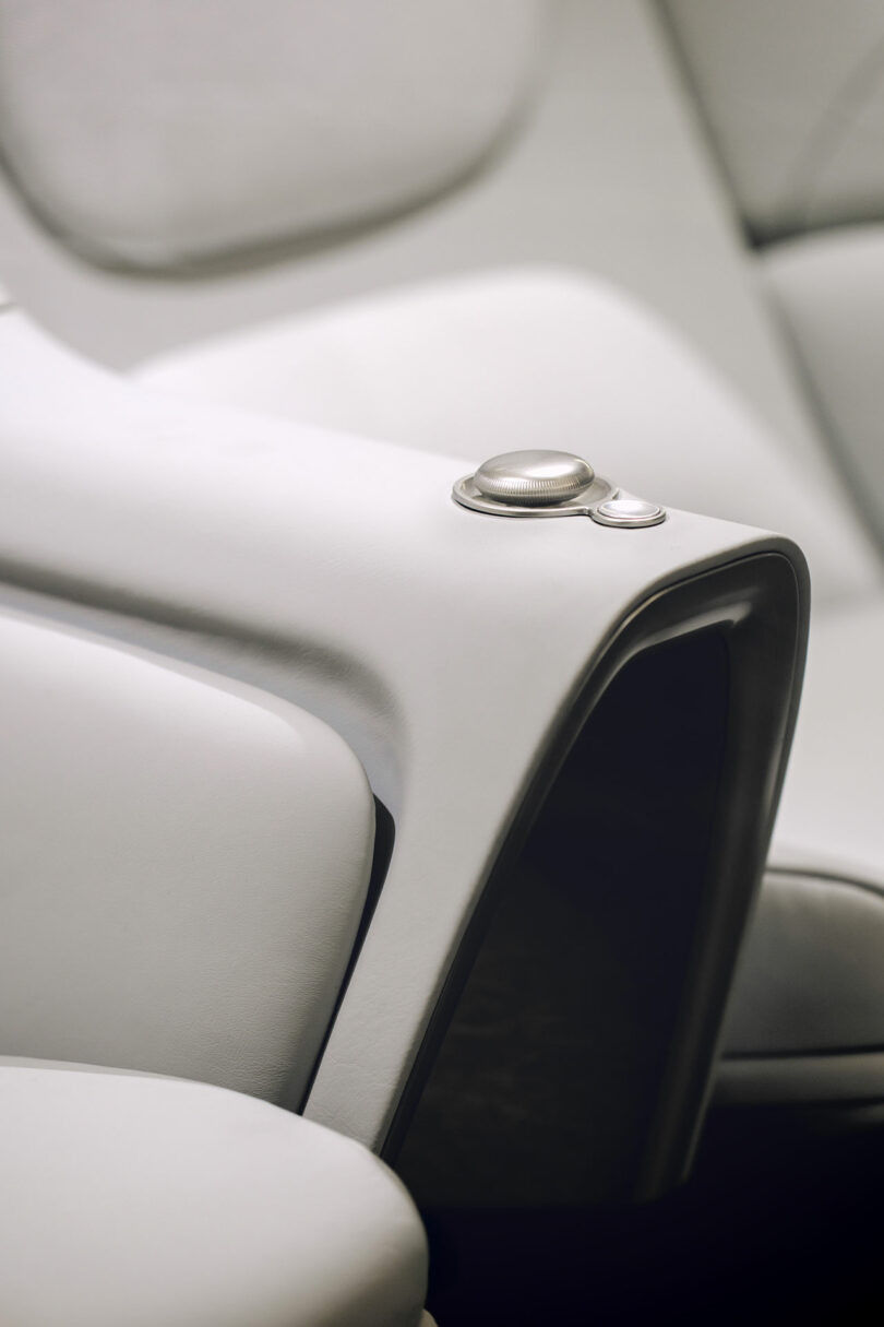 Primer plano de un moderno asiento de cuero blanco con perillas de control metálicas integradas en el reposabrazos.