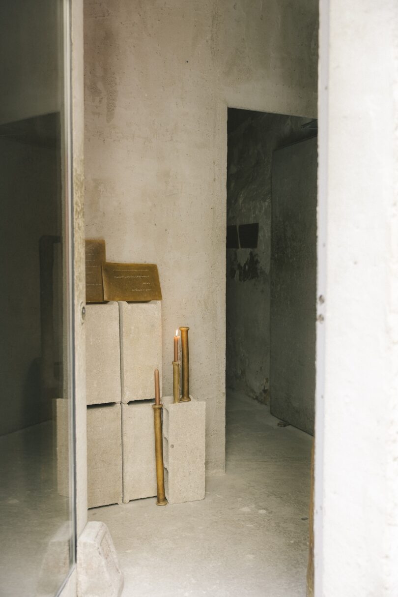 Una habitación pequeña y sencilla con piedras, una placa y algunas velas encendidas en las piedras y en el suelo cerca de la entrada.