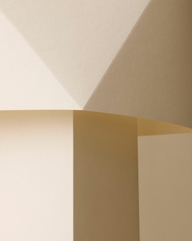 Formas geométricas formadas por la superposición de papeles beige, creando ángulos agudos y sombras sutiles.