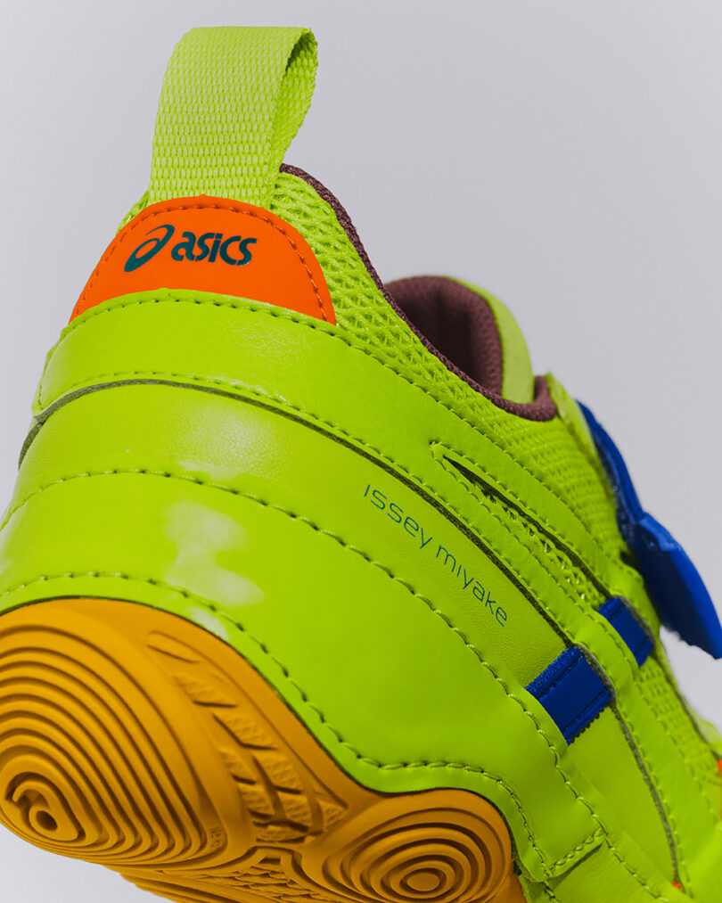 Primer plano de zapatillas Asics de color verde neón con detalles en azul, detalles en naranja y amarillo y "issey miyake" Impreso en el lateral.