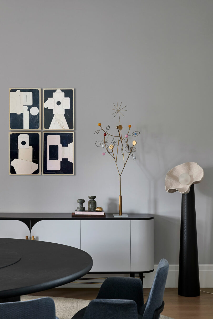 Salón moderno con arte abstracto en la pared, decorado con esculturas doradas, libros y una consola blanca; una escultura alta se encuentra a la derecha.