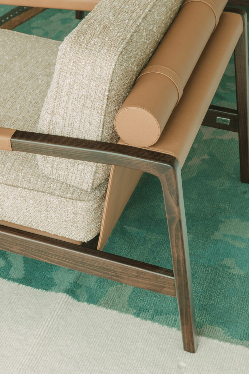 Wood-framed armchair with tan leather and textured beige cushions, placed on a teal patterned rug.