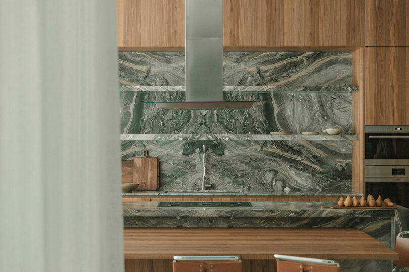 Modern kitchen with wood cabinets, a marble backsplash and countertop, stainless steel range hood, and minimalist decor.