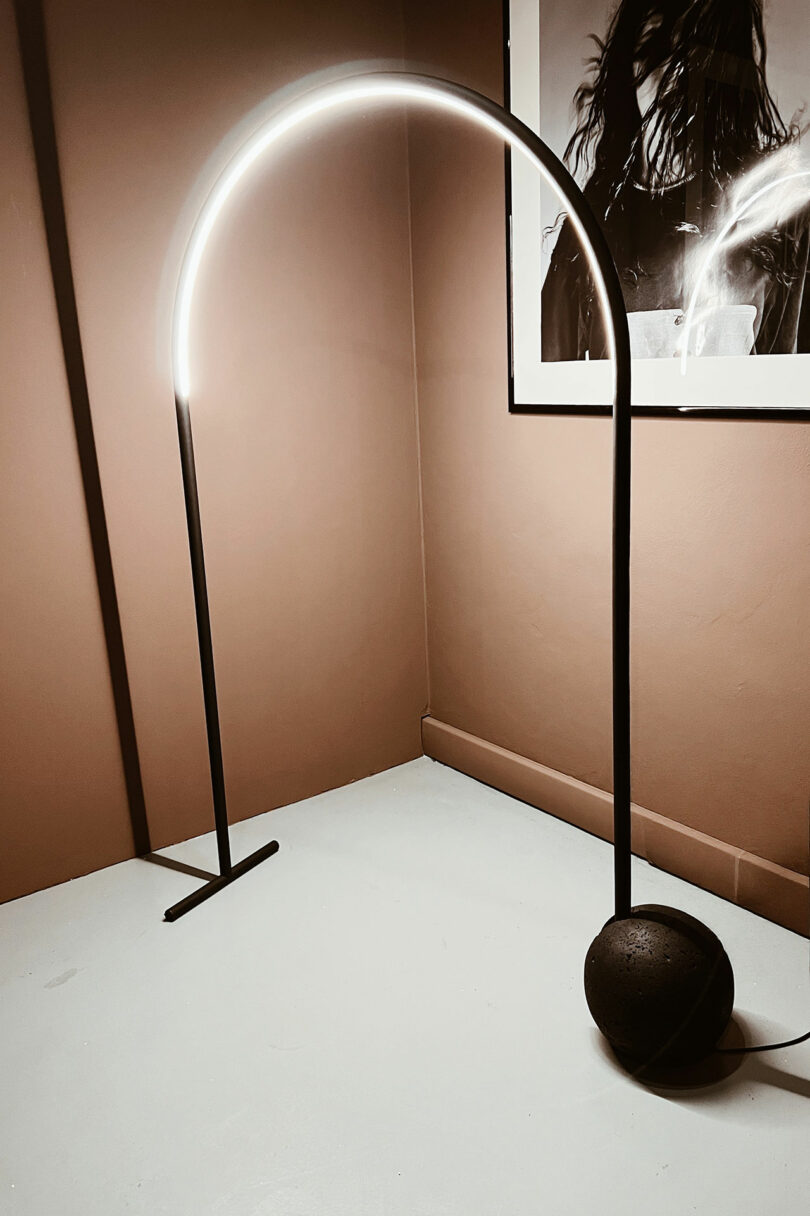 A modern arched floor lamp with a glowing LED light stands in a corner near a wall-mounted black-and-white portrait, creating a serene space to relax and Take 5.