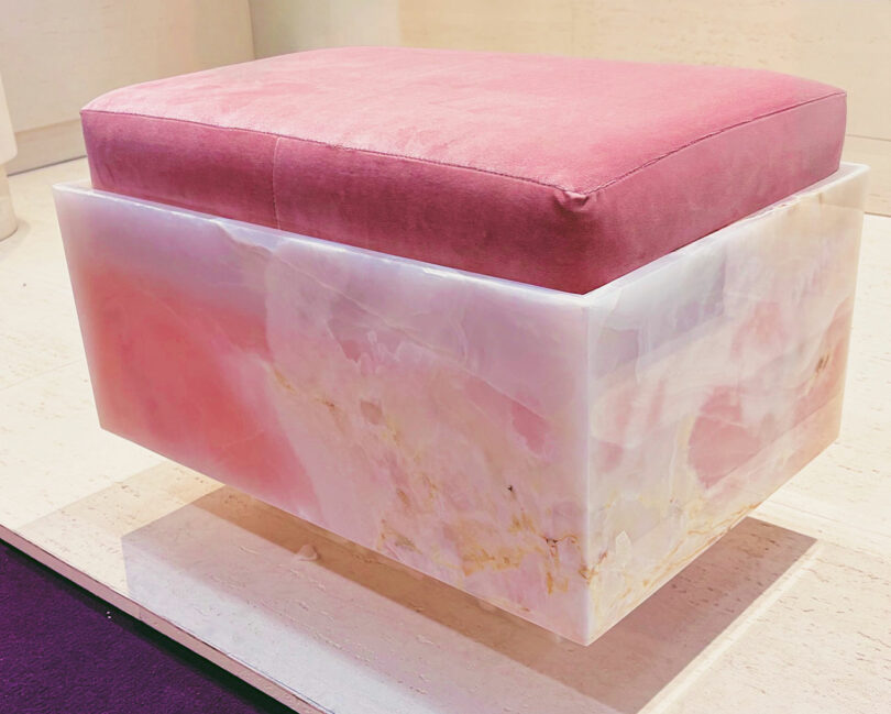 A square ottoman, featuring a polished pink onyx base and a plush pink velvet cushion, elegantly placed on a light-colored floor.