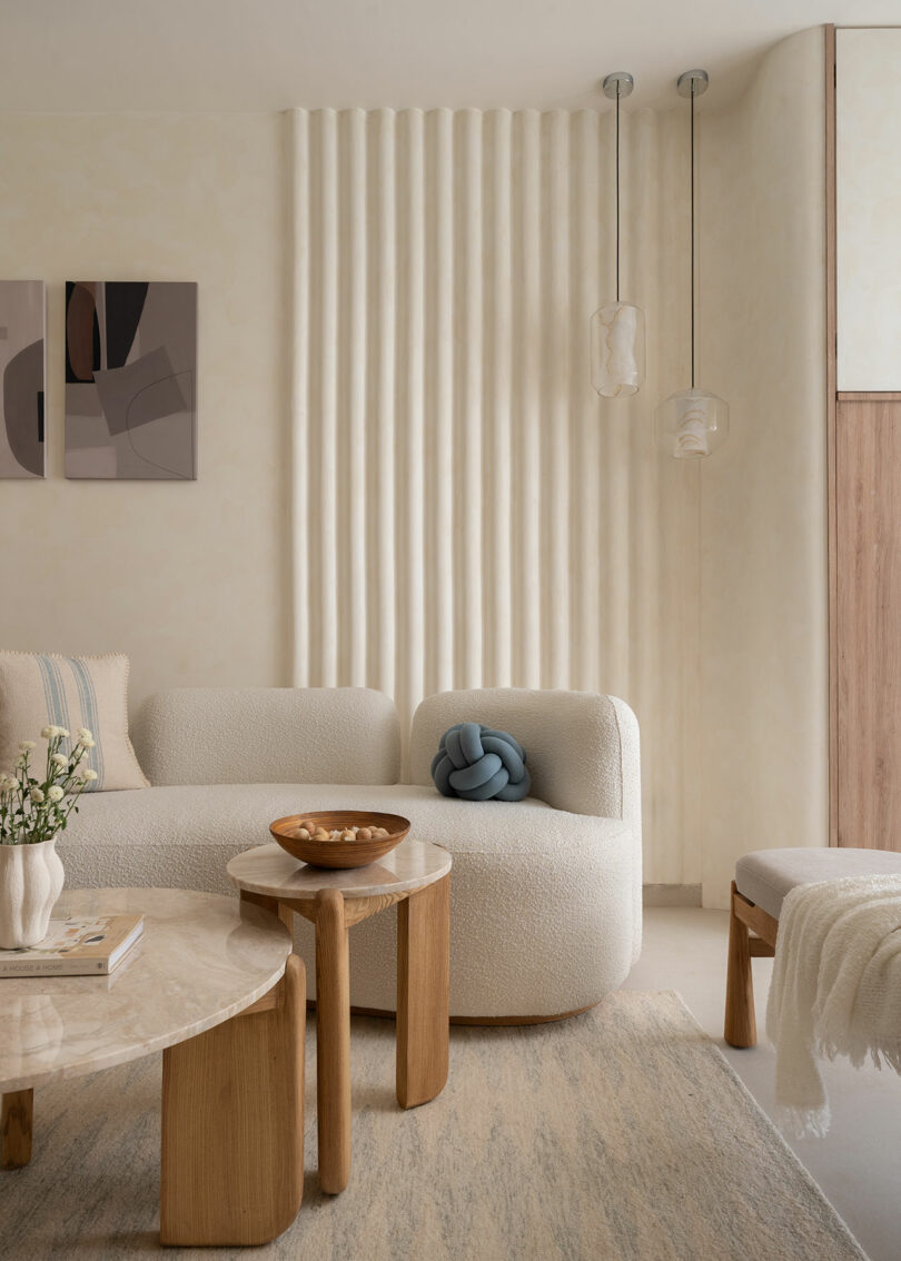 Salón minimalista con muebles de textura beige, mesa de madera, arte abstracto en la pared, lámpara de araña y pared acanalada. La decoración se basa en colores neutros y beige.